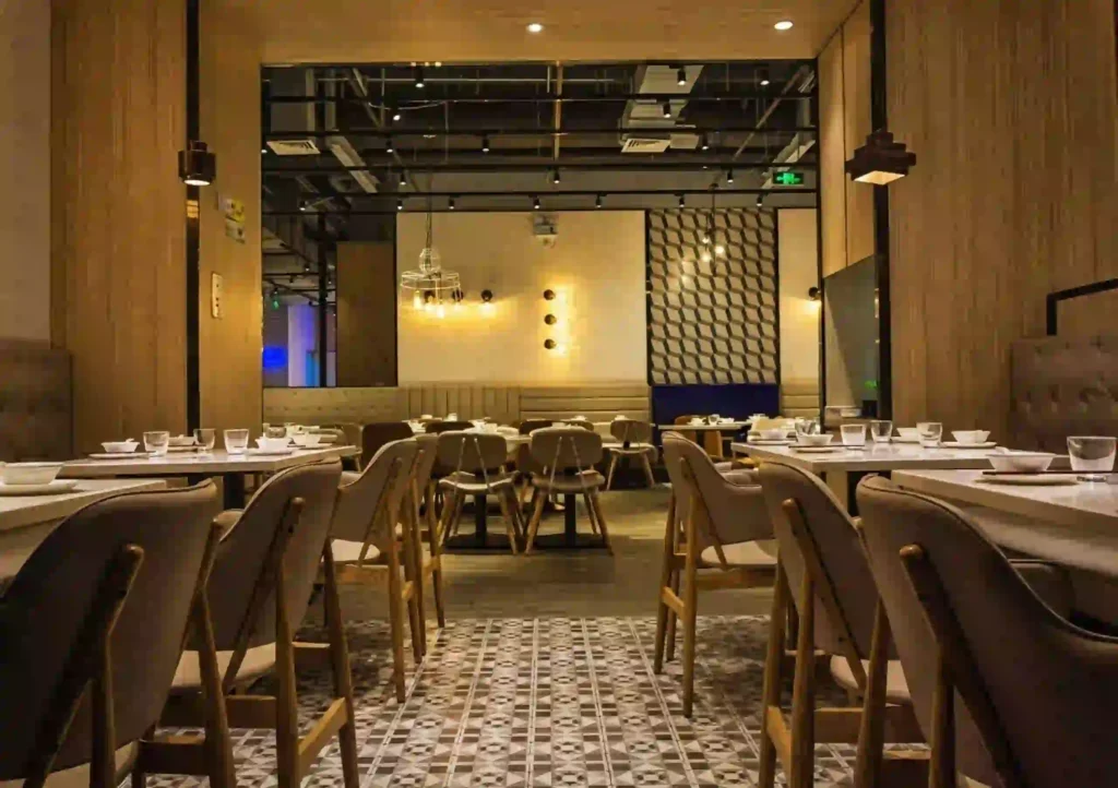 Modern restaurant dining hall featuring custom vertical wooden paneling, geometric floor tiles, and warm hanging pendant lights in a commercial fitout setting.